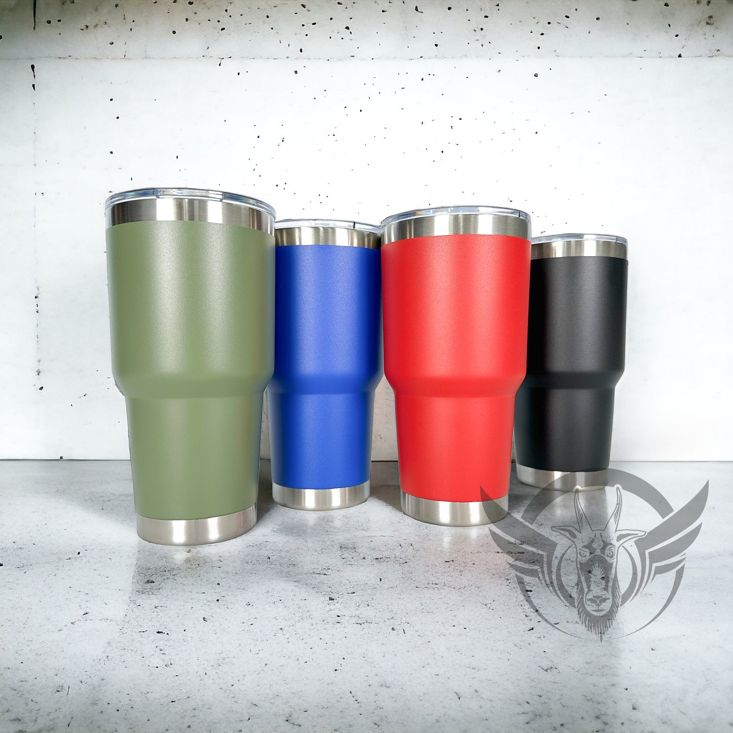 Four, plain, 30 ounce tumblers in green, blue, red and black are placed next to one another, respectively, to show all available color options to choose from. Cups are displayed on concrete surface with white background.