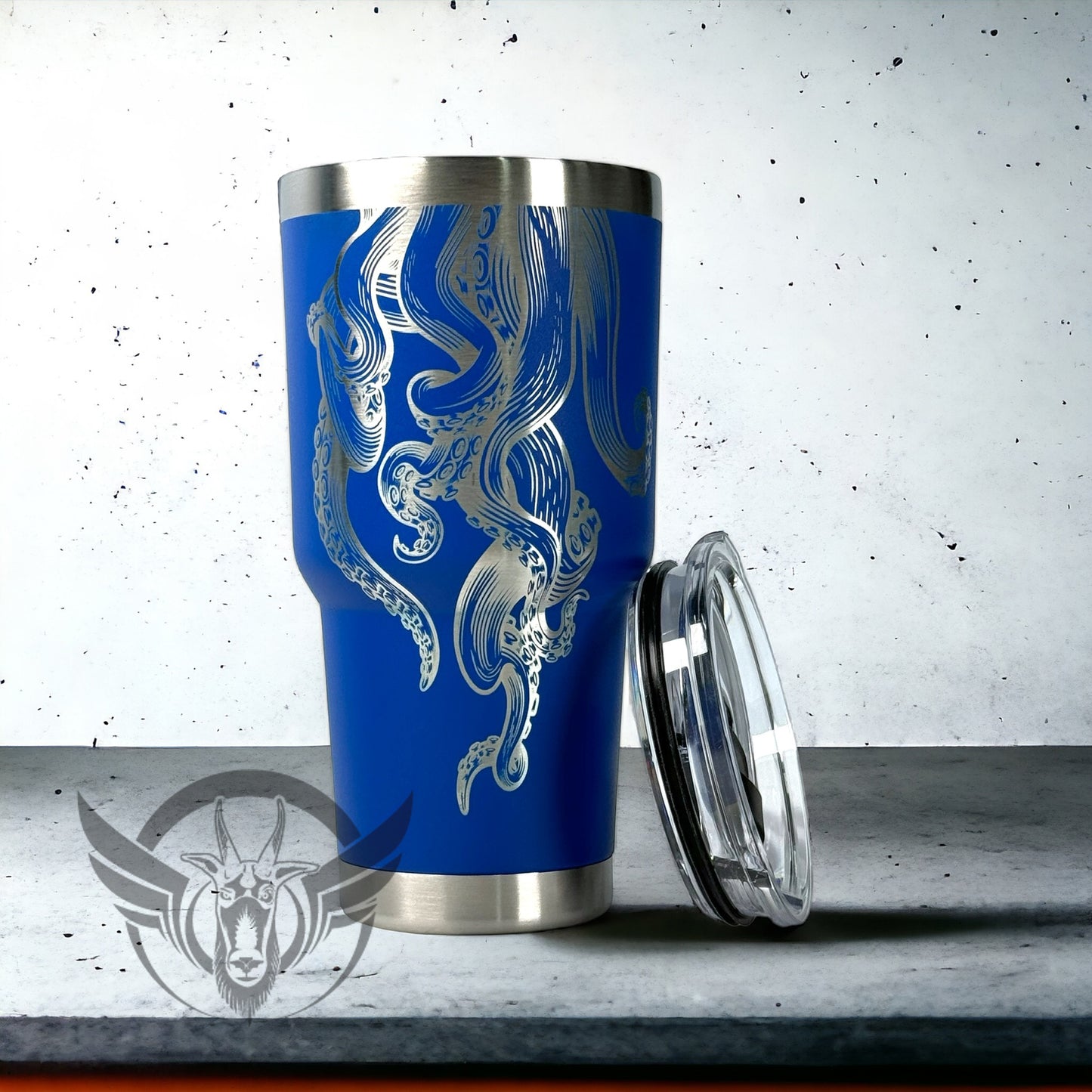 A bright blue 30 ounce tumbler is shown with its lid leaning against it. The cup has a detailed tentacle design coming from the top to the bottom. The cup is displayed on a cement surface with white background.