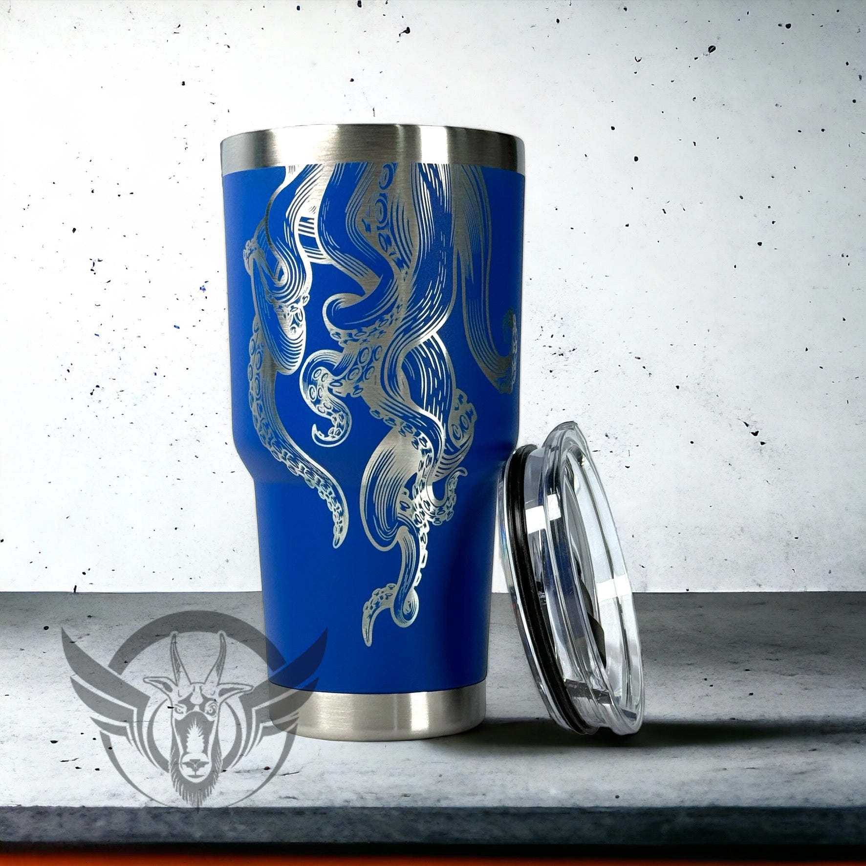 A bright blue 30 ounce tumbler is shown with its lid leaning against it. The cup has a detailed tentacle design coming from the top to the bottom. The cup  is displayed on a cement surface with white background.